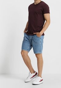 Kastanjebrun crew neck t-shirt, blå denimshorts med fickor och vita sneakers med röda och blå detaljer. Avslappnad outfit.