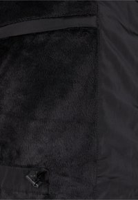 Svart hybridstoff med myk, teksturert fleece ved siden av en glatt, matt polyester. Inkluderer en sidelomme med låsespenn.