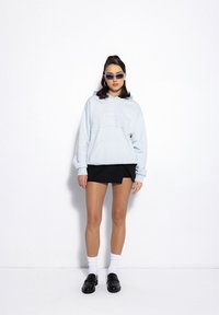 Jasnoniebieska bluza z kapturem z tłoczonym napisem, noszona z czarną spódnicą. Połączona z czarnymi loafersami i białymi skarpetkami do kostek, a także uzupełniona okularami przeciwsłonecznymi.