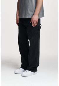 Czarne spodnie cargo o luźnym kroju, z bocznymi kieszeniami i teksturowaną tkaniną. Połączone z białymi trampkami.