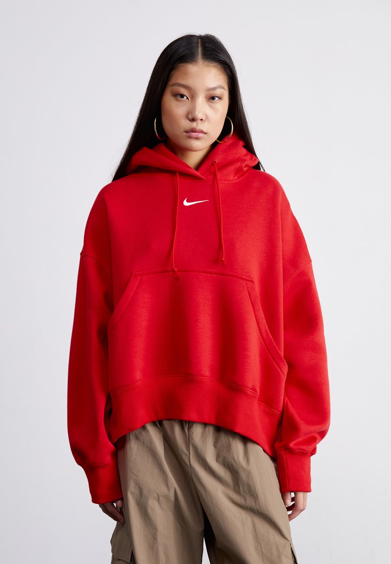 Piros Nike kapucnis pulóver elülső zsebbel, állítható húzózsinórral és bordázott mandzsettákkal. A mellkasán fehér Nike logó található.