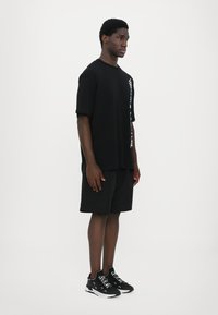 Svart oversized T-skjorte med sidetrykk, kombinert med svarte shorts og svarte sneakers med hvite detaljer, glatt stoff, avslappet passform.