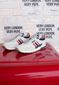 Sive mrežaste tenisice s plavim i crvenim akcentima, s tri pruga sa strane, teksturiranom potplatom i logotipom na jeziku.