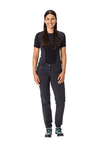 Crna atletska majica s mrežastim panelima i tamnim suženim hlačama, koje imaju patentne zatvarače i džepove. Par tirkiznih planinarskih čizama upotpunjuje outfit.