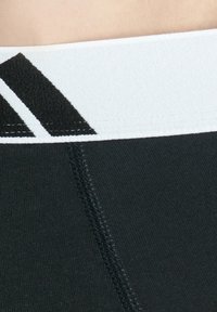 Fascia elastica nera per allenamento con una banda contrastante bianca caratterizzata da strisce diagonali nere. Texture liscia e cuciture piatte per il comfort.