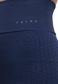 Granatowe, dziane legginsy z teksturowanym panelem przedstawiającym geometryczny wzór. Nazwa marki "FALKE" widoczna na szarej gumie w talii.