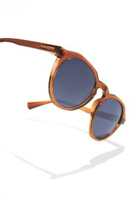 Kulaté sluneční brýle s obrubou z želvoviny, modře tónovanými čočkami a zlatým logem na rameni. Hladké hranice a pevné nožičky.