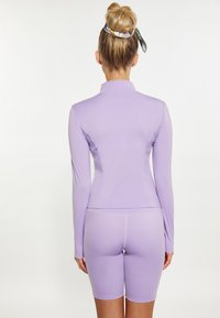 Set de îmbrăcăminte activă de culoare lila, compus dintr-un top cu mânecă lungă și guler înalt, împreună cu pantaloni scurți asortați. Textură netedă și design ajustat.