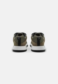 Buty sportowe z zieloną cholewką, czarnymi akcentami i białą podeszwą. Posiadają teksturowane materiały oraz tylną pętlę ułatwiającą zakładanie.