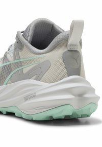 Scarpa da corsa grigio chiaro con tomaia in mesh, dettagli in menta, suola resistente, particolare testurizzato sul tallone e logo riflettente sul lato.