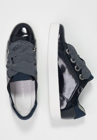 Baskets bleu marine en cuir verni brillant, lacets en tissu rayé, col rembourré et semelle en caoutchouc blanche. Accents latéraux dans des tons assortis.