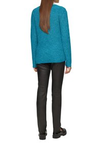 Türkisfarbener gestrickter Pullover mit strukturiertem Muster, kombiniert mit schwarzen Lederhosen. Schlichtes Design, lange Ärmel und lockere Passform.