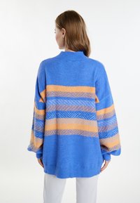 Maglione oversize blu a maglia con motivi a strisce arancioni e blu, caratterizzato da un collo alto e polsini a coste. Tessuto morbido.
