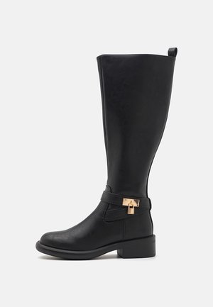 Botte noire mi-mollet avec talon bloc bas, détail décoratif en métal doré en forme de verrou sur la sangle autour de la cheville, en cuir lisse.