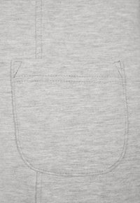 Szara kieszeń materiałowa o zaokrąglonym kształcie, z podszytym brzegiem i miękką fakturą, będąca częścią projektu ubrania.