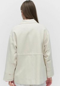 Ljusbeige oversized jacka med en strukturerad krage, långa ärmar och synliga sömdetaljer på baksidan. Mjuk, texturerad tyg.