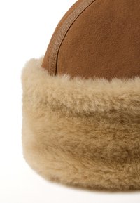Bruin suede hoed met een zachte, beige bont gevoerde rand. De textuur is pluche, in contrast met de gladde buitenkant van de hoed.