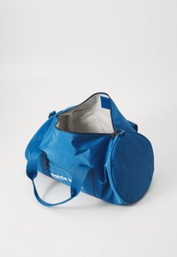 Blaue Sporttasche aus glattem Nylon mit einem Reißverschluss oben, zwei stabilen Griffen und weißem Branding auf einer Seite. Das Innere ist beige.