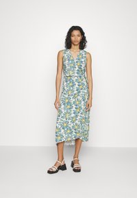Robe portefeuille florale avec décolleté en V, sans manches, en tissu léger avec des motifs bleus, verts et jaunes, et un ourlet asymétrique.
