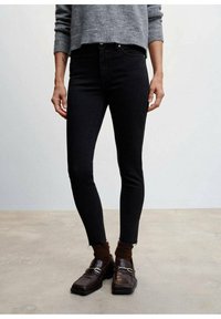 Jeans negros ajustados con una cintura alta y un corte slim. Combinados con mocasines marrones y calcetines marrones acanalados, con detalles sutiles en los zapatos.