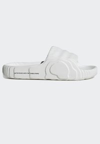 Vit slid sandal med ribbad yta. Har ett brett band över toppen och en konturerad fotbädd. Inkluderar tryckt logotyp på sidan.