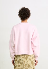 Felpa corta rosa con spalle scese e polsini a coste, abbinata a una gonna con motivo camouflage. Materiale morbido, vestibilità casual.
