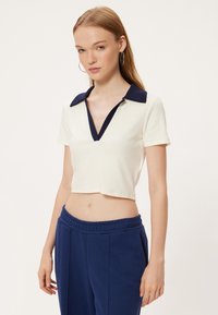 Geknipte witte top met marineblauwe kraag en V-hals ontwerp, korte mouwen, textuurstof. Gecombineerd met marineblauwe broek met trekkoord.