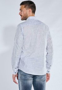 Langärmliges Hemd in hellgrau mit dezenten vertikalen Streifen, Button-Down-Kragen und schwarzen Knopf-Akzenten an den Manschetten. Der Stoff wirkt leicht.