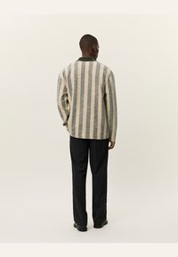 Pulover tricotat cu dungi verticale crem și gri, design cu guler, fit relaxat, purtat peste pantaloni negri, evidențiind țesătura texturată.