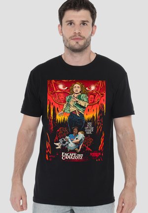 Man wearing black t-shirt with colorful Stranger Things poster art showing characters running from glowing eyes in dark forest.