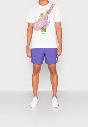 T-shirt bianco con una grafica colorata, pantaloni corti viola, borsa in vita rosa e sneakers bianche con un delicato accento blu.