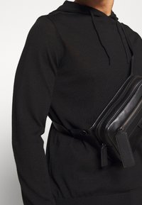 Czarny kapturowy sweter o fakturowanym wykończeniu oraz czarna skórzana torba na ramię z zamkami i akcentami w postaci metek.