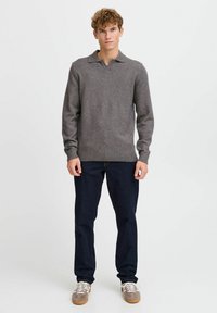 Grauer Strickpullover mit einem Kragen, gerippten Bündchen und Saum. Trägt man mit dunkelblauen Jeans und grauen Turnschuhen. Minimalistisches Design.
