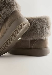 Suède enkellaarsjes met een zachte, fluffy grijze bontkraag, beige tinten en een gestructureerde rubberen zool met een golvend patroon.