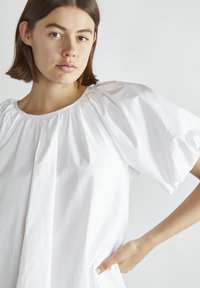 Hvid bluse med rund halsudskæring, puffede ærmer og blødt, letvægtsstof med en glat tekstur. Enkel og moderne design.