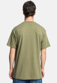 Camiseta de algodón de color verde oliva con mangas cortas, cuello redondo y un ajuste relajado, mostrada desde la parte posterior con una textura sólida.