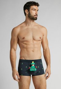 Černé boxerky se zeleným vzorem vánočního stromku, s plyšovou zelenou postavičkou a žlutou hvězdou nahoře vpředu.