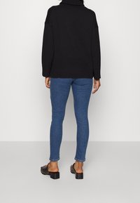 Svart oversized tröja med hög krage och ribbad nederkant, kombinerad med åtsittande blå jeans och svarta klackskor med blockklack.