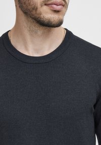 Mörk marinblå stickad tröja med rundad halsringning och subtila ribbade detaljer vid halsen, som har en slät textur och en figurnära design.