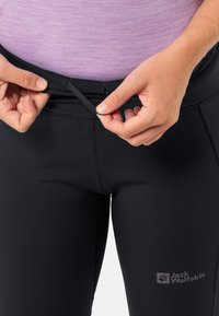 Zwarte leggings met een gladde textuur en een nauwsluitend ontwerp. Een tailleband heeft een trekkoord voor aanpassing. Jack Wolfskin-logo nabij de zoom.