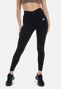 Svart high-waisted leggings i en slät, elastisk tyg, med en vit logotyp på höften och en sömlös design för komfort.