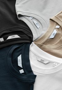Quatre T-shirts en noir, marine, blanc, gris clair et beige. Encolures rondes, coupe décontractée, en coton. Étiquettes visibles avec le nom de la marque.