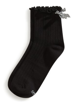 Chaussettes courtes côtelées noires avec bords volants et petit nœud à carreaux noir et blanc sur le côté.