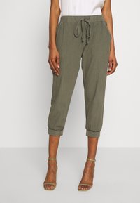 Pantalon fuselé vert olive avec poignets élastiques, taille à cordon de serrage et poches latérales, fabriqué en tissu léger à finition texturée.