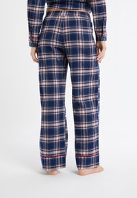 Granatowe flanelowe spodnie piżamowe w kratę w białe i czerwone wzory. Posiadają elastyczny pas i proste nogawki z czerwonymi akcentami na dole.
