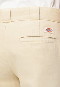 Beige auduma bikses ar teksturētu virsmu, ar aizmugures kabatu un mazu Dickies logo uzšūtu uz jostas.