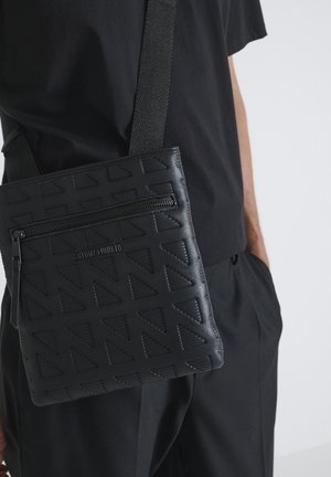 Borsa a tracolla in pelle nera con motivo geometrico a sbalzo, tasca frontale con zip e tracolla texturizzata.