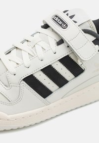 Vita lädersneakers med svarta mocka- och läderdetaljer, som har tre svarta ränder, ett kardborreband och en texturerad gummisula.