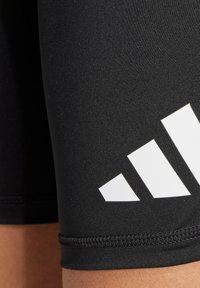 Schwarze Sportshorts aus elastischem Material mit glatter Textur. Mit einem großen weißen Adidas-Logo am Oberschenkel und Flachnahtnähten.
