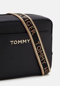 Czarna prostokątna torba z złotym logo "TOMMY". Posiada wzorzystą rączkę w kolorze czarnym z złotymi i brązowymi akcentami. Gładka, fakturowana powierzchnia.